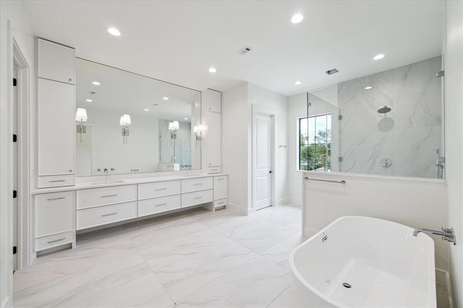 The primary bathroom features a double door entry and includes a Wyndham Collection Carissa freestanding acrylic soaking tub. The walk-in shower boasts seamless glass walls and a door, complemented by designer chrome plumbing fixtures. A custom white oak vanity with double sinks, a wall-mounted designer chrome faucet, and quartz countertops provide both elegance and functionality. Additional highlights include designer sconce lighting and a makeup vanity with knee space.