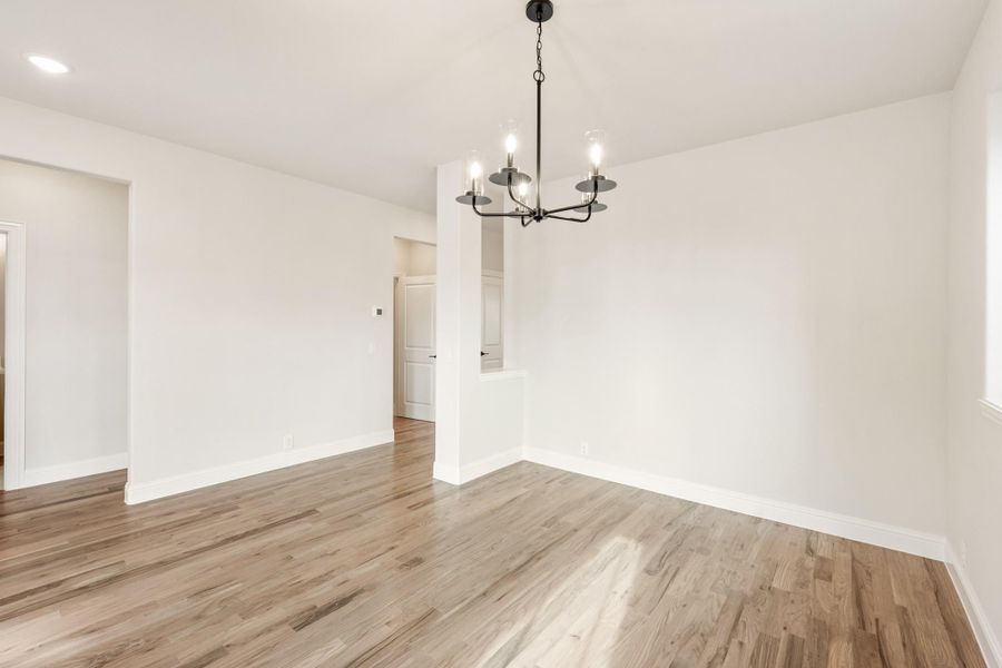 Empty dining room with hardwood floors, white walls, and a black metal chandelier overhead.