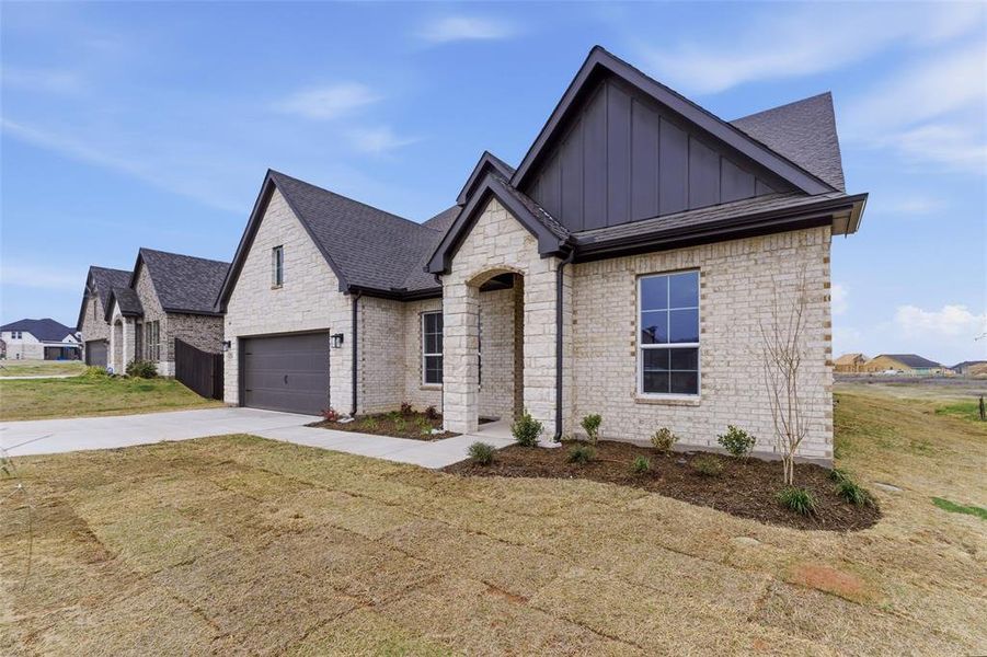 View of front of home with board and batten siding, concrete driveway, stone siding, a front yard, and brick siding