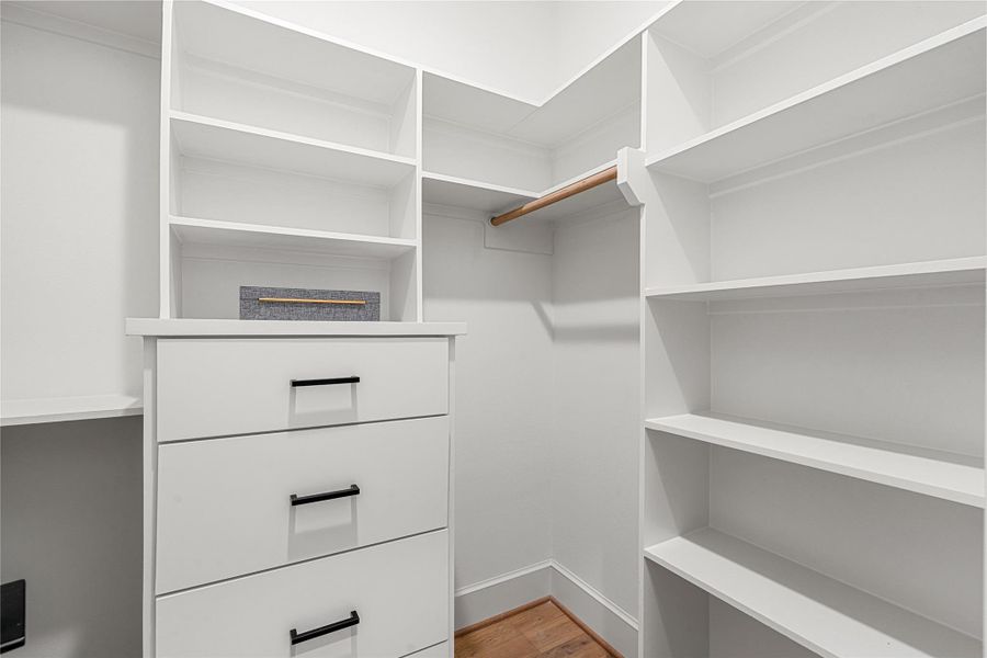 Spacious walk-in closet featuring white shelving and drawers, a spaces to hanging clothes, and ample storage on both sides. Perfect for organizing clothing and accessories.