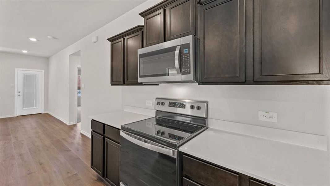 Kitchen area featuring dark wood-finish cabinetry, stainless steel appliances, solid surface countertops, and wood-finish flooring