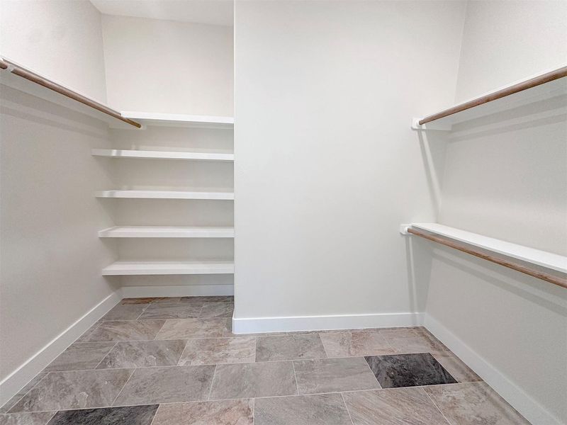 Walk in closet featuring excellent hanging rod spacew and. storage shelves, stone finish flooring