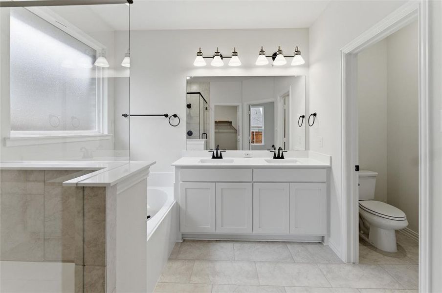 Bathroom featuring a dual vanity with white cabinetry and undermount sinks, a large framed mirror, and a built-in bathtub with tiled surround