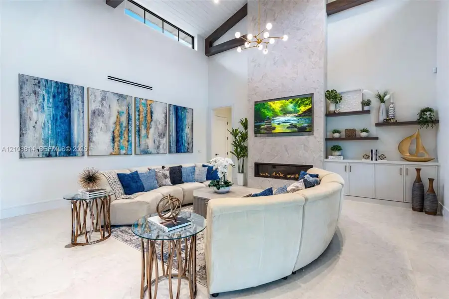 Vaulted ceiling with exposed wood beams, floor-to-ceiling stone-surround fireplace, linear electric firebox, clerestory windows, and built-in lower cabinetry with floating wall shelves Vaulted ceiling with exposed wood beams, floor-to-ceiling stone-surround fireplace, linear electric firebox, clerestory windows, and built-in lower cabinetry with floating wall shelves