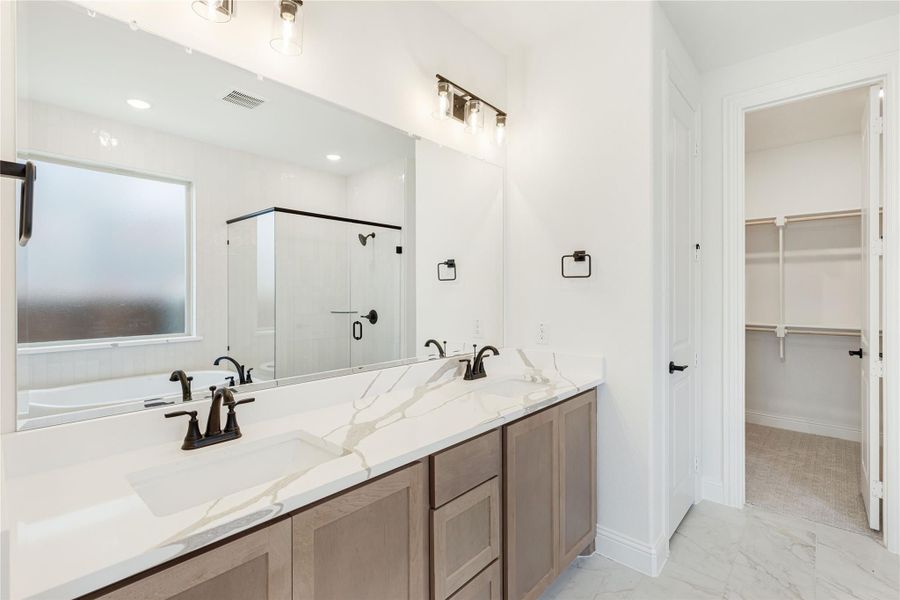Bathroom with double vanity, quartz countertop, wood cabinets, glass shower, and walk-in closet entrance