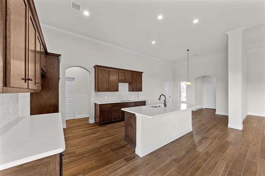 Kitchen with crown molding, a center island with sink, hanging light fixtures, and sink