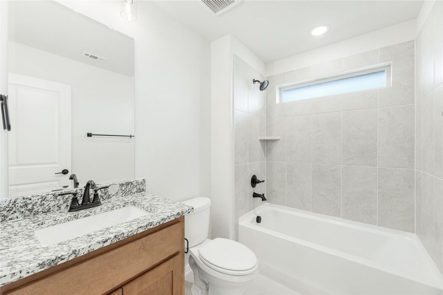 Bathroom with granite countertop vanity, white tub-shower combo with tile surround, and black fixtures