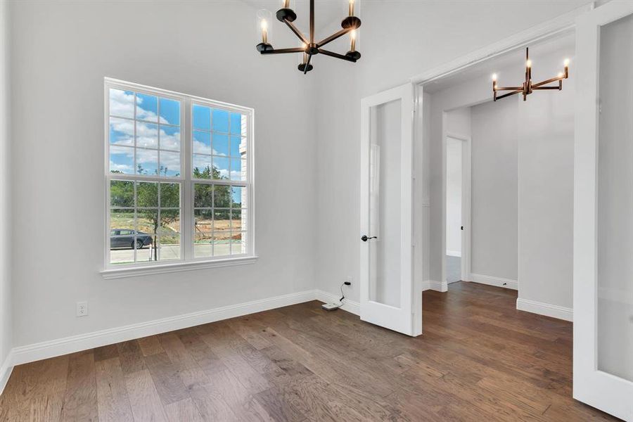 Spare room featuring an inviting chandelier, wood-type flooring, and a towering ceiling