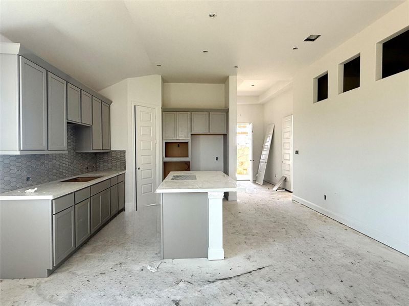Kitchen featuring vaulted ceiling, gray cabinetry, a kitchen island, and tasteful backsplash Kitchen featuring vaulted ceiling, gray cabinetry, a kitchen island, and tasteful backsplash