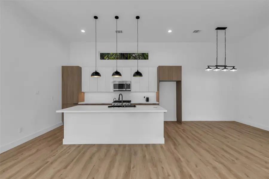 Elegant light fixtures illuminate the kitchen and dining area, while white walls pair beautifully with the warm beige floors to create a bright and welcoming atmosphere. Elegant light fixtures illuminate the kitchen and dining area, while white walls pair beautifully with the warm beige floors to create a bright and welcoming atmosphere.