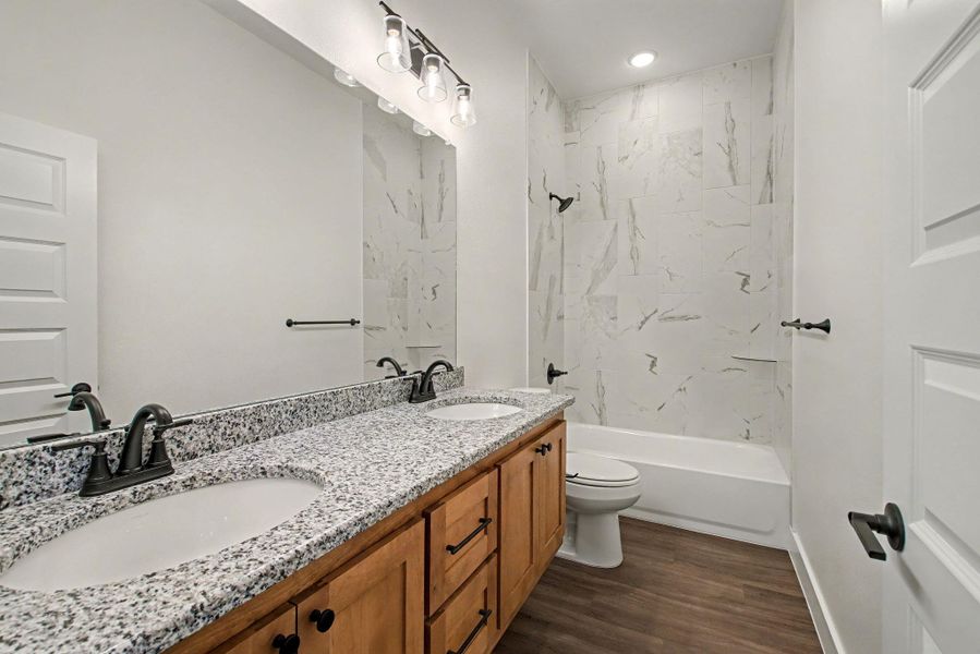 Bathroom with double vanity, shower / washtub combination, and dark wood-style flooring