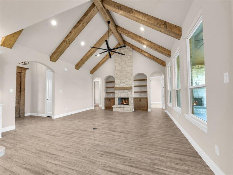 Unfurnished living room featuring beam ceiling, ceiling fan, a stone fireplace, high vaulted ceiling, and hardwood / wood-style flooring