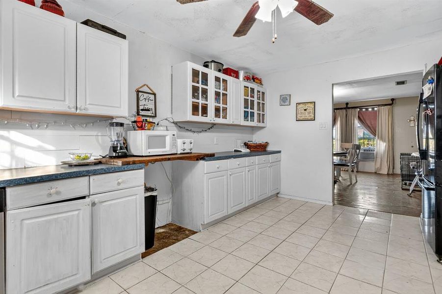 Kitchen featuring a barn door, dark countertops, glass insert cabinets, light tile patterned floors, and white cabinets Kitchen featuring a barn door, dark countertops, glass insert cabinets, light tile patterned floors, and white cabinets