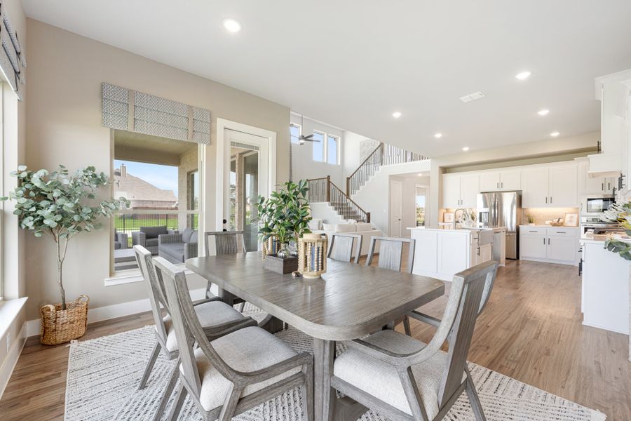 Open-concept dining area with gray wood table, six chairs, and view of white kitchen and staircase beyond.