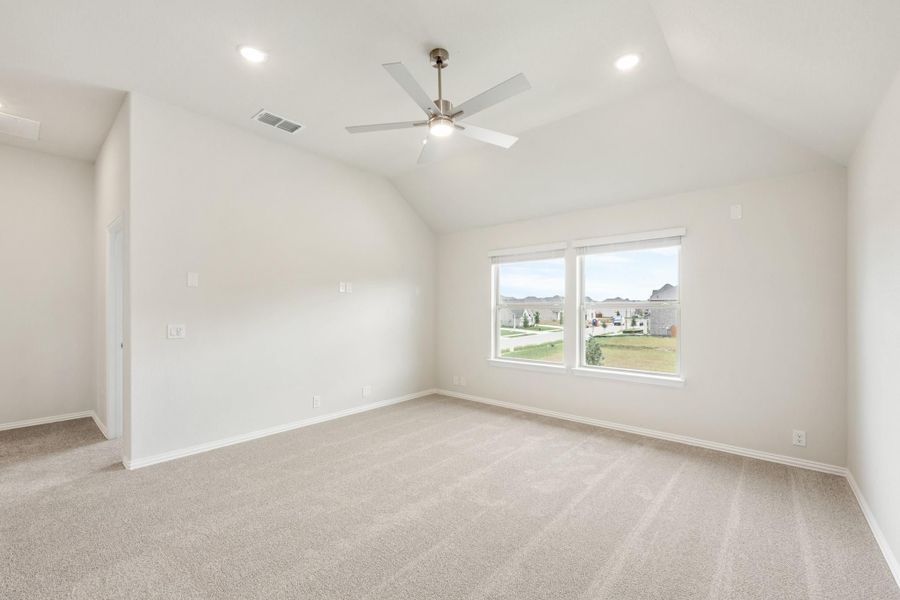 Empty bedroom with vaulted ceiling, ceiling fan, carpet flooring, and a window overlooking the neighborhood