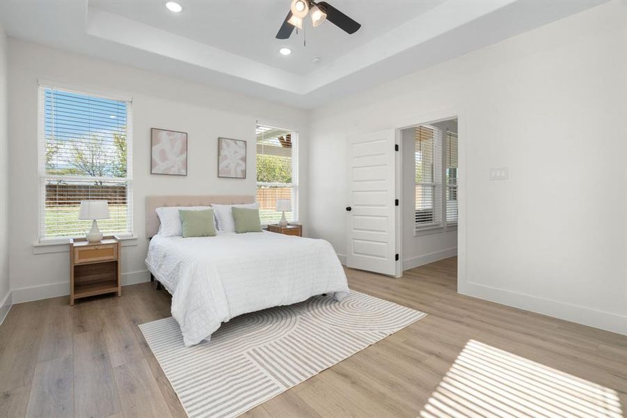 Bedroom with light wood-type flooring, ceiling fan, recessed lighting, and a raised ceiling Bedroom with light wood-type flooring, ceiling fan, recessed lighting, and a raised ceiling