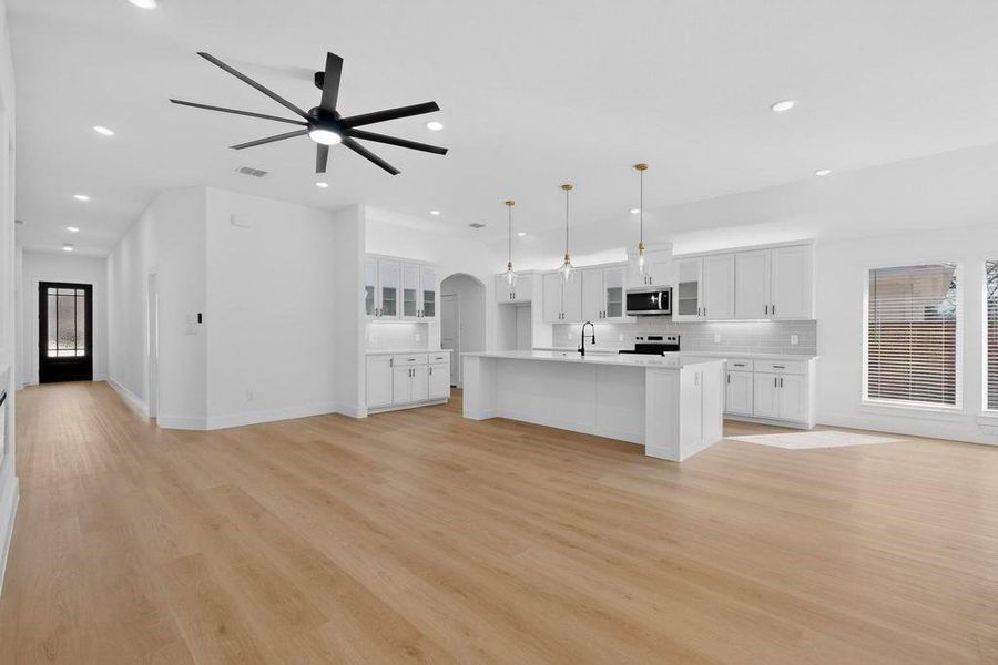 Unfurnished living room featuring arched walkways, ceiling fan, light wood-style flooring, and recessed lighting