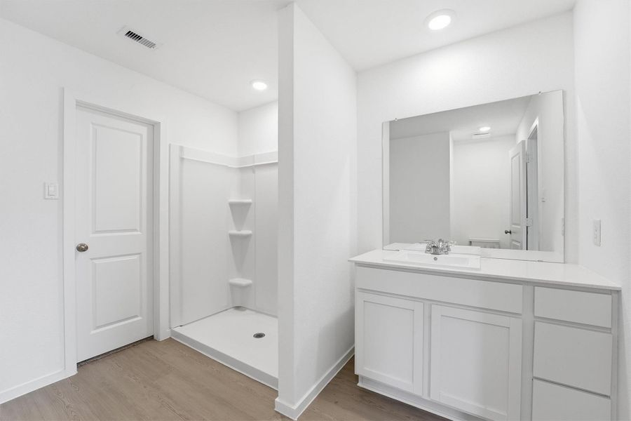 This bathroom features a modern, minimalistic design with a spacious walk-in shower, sleek white vanity with ample storage, and bright lighting, creating a clean and inviting space.