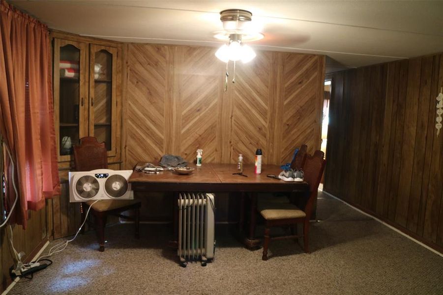 Carpeted dining space featuring radiator heating unit, wood walls, and ceiling fan Carpeted dining space featuring radiator heating unit, wood walls, and ceiling fan