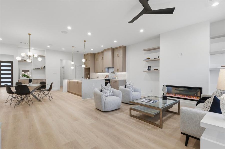 Living room with suspended lighting, light wood-style flooring, a glass covered fireplace, and ceiling fan Living room with suspended lighting, light wood-style flooring, a glass covered fireplace, and ceiling fan