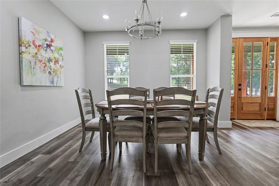 Dining area featuring wood-finish flooring, two large windows with blinds, recessed lighting, and a chandelier