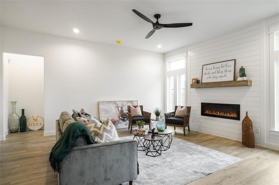 Living room with ceiling fan, light wood-type flooring, and a large fireplace