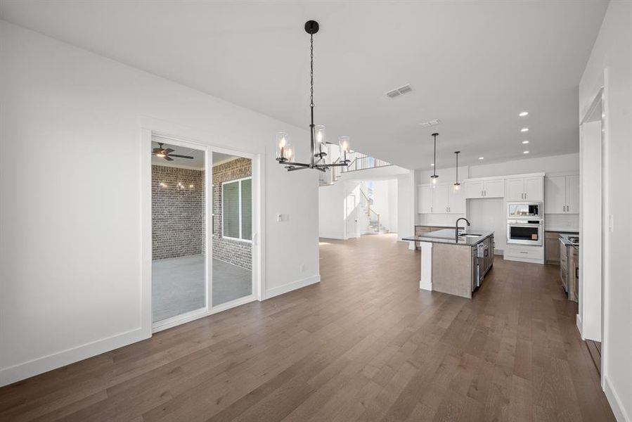 Kitchen featuring open floor plan, white cabinetry, a center island with sink, hanging light fixtures, and a chandelier