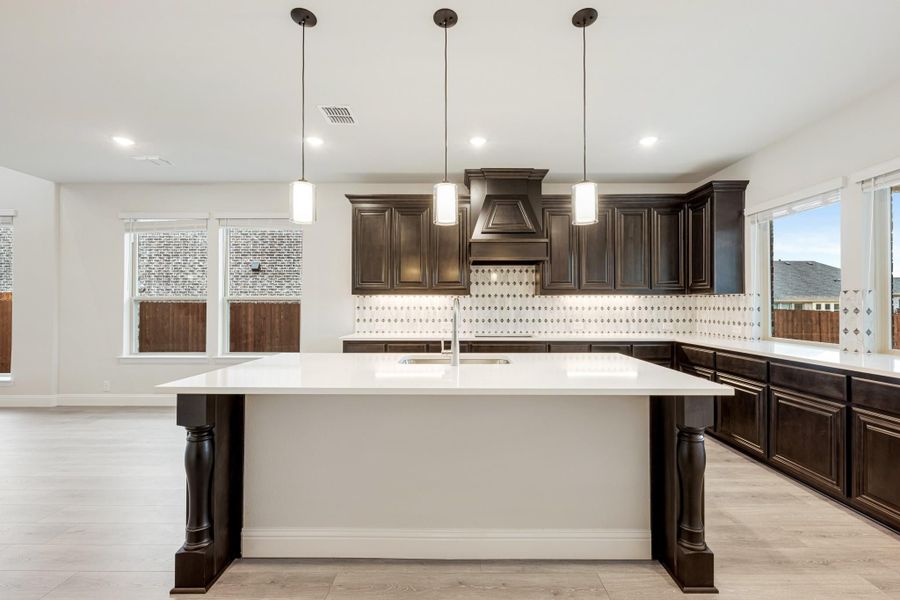 Kitchen with large white island, dark wood cabinets, patterned tile backsplash, and three pendant lights