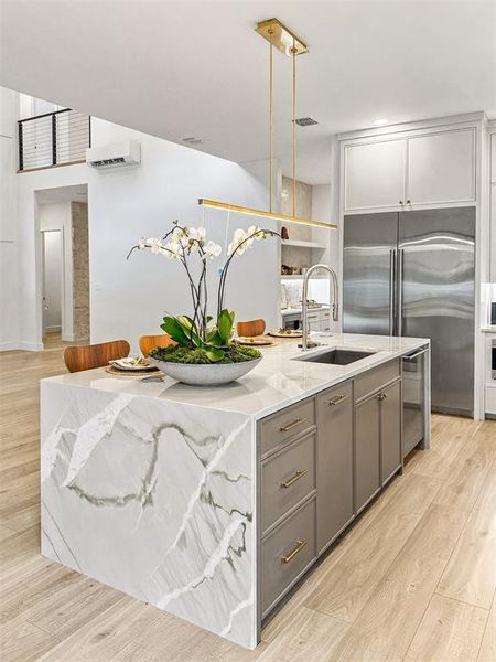Kitchen with gray cabinets, appliances with stainless steel finishes, light wood-type flooring, and a center island with sink