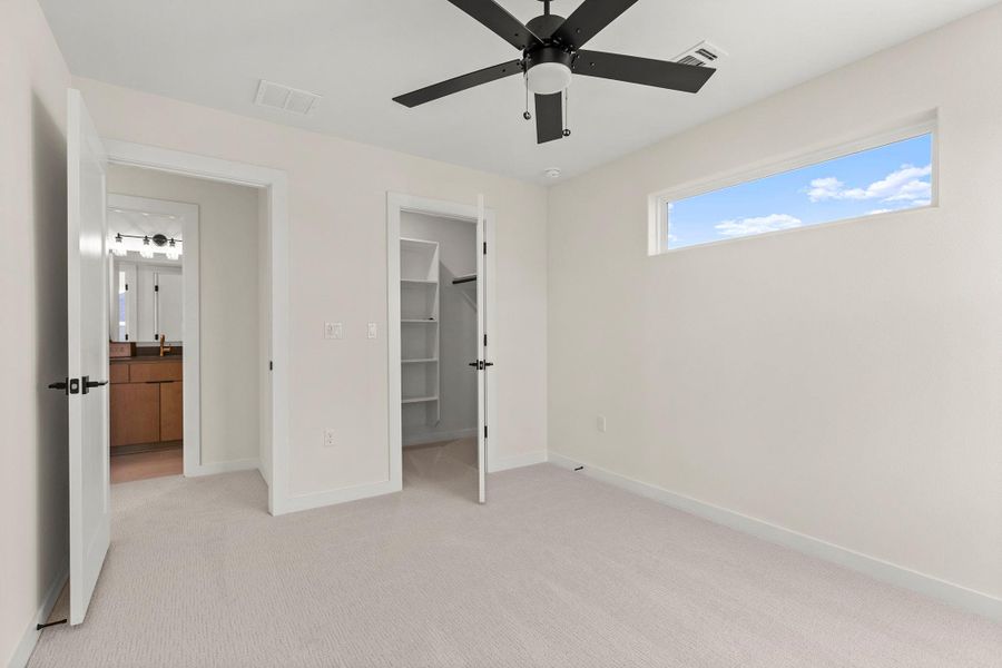 Unfurnished bedroom with a walk in closet, light colored carpet, and ceiling fan