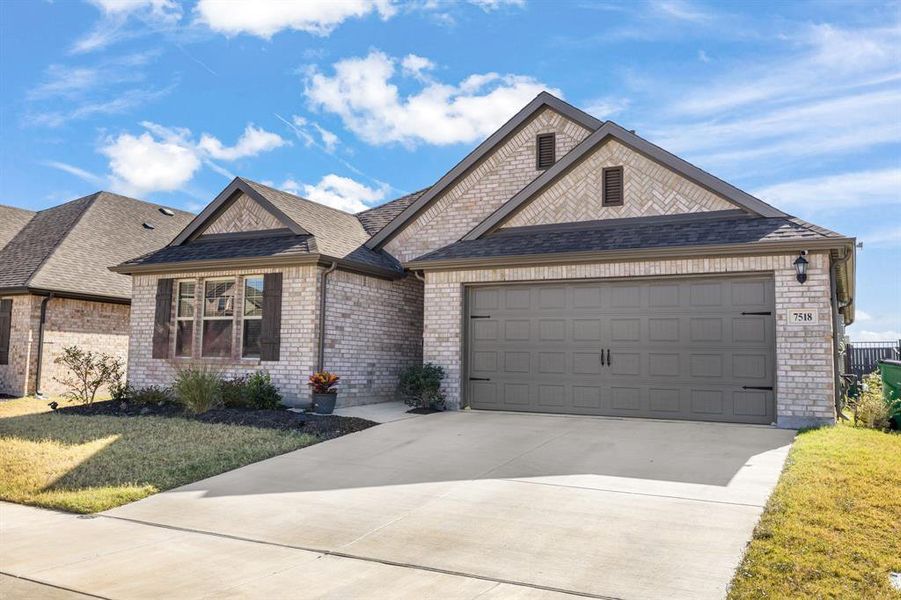 French provincial home featuring a shingled roof, driveway, brick siding, an attached garage, and a front yard French provincial home featuring a shingled roof, driveway, brick siding, an attached garage, and a front yard