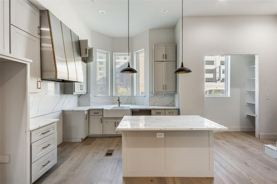 Kitchen featuring full height quartz backsplash, center island, custom hood, and engineered wood flooring.  This home is under construction and not the Residence for sale.