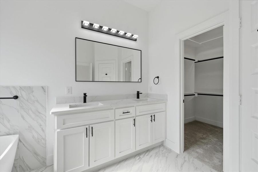 Primary Full bath with double vanity, light marble finish flooring, a freestanding tub, and a walk in closet