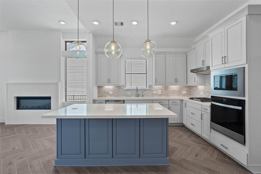 The kitchen anchors the space with a stunning powder-blue island contrasted by crisp white cabinetry. This designer space is fully equipped with premium stainless steel appliances and expansive white quartz countertops that provide a sleek, durable surface for both culinary prep and casual entertaining.