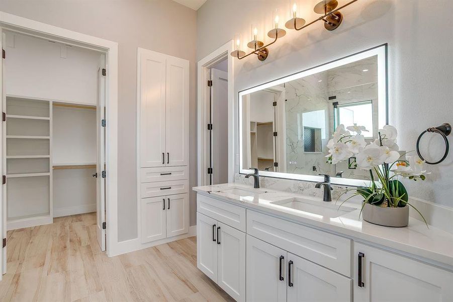 Bathroom with a walk in closet, double vanity, light wood-style flooring, and a marble finish shower