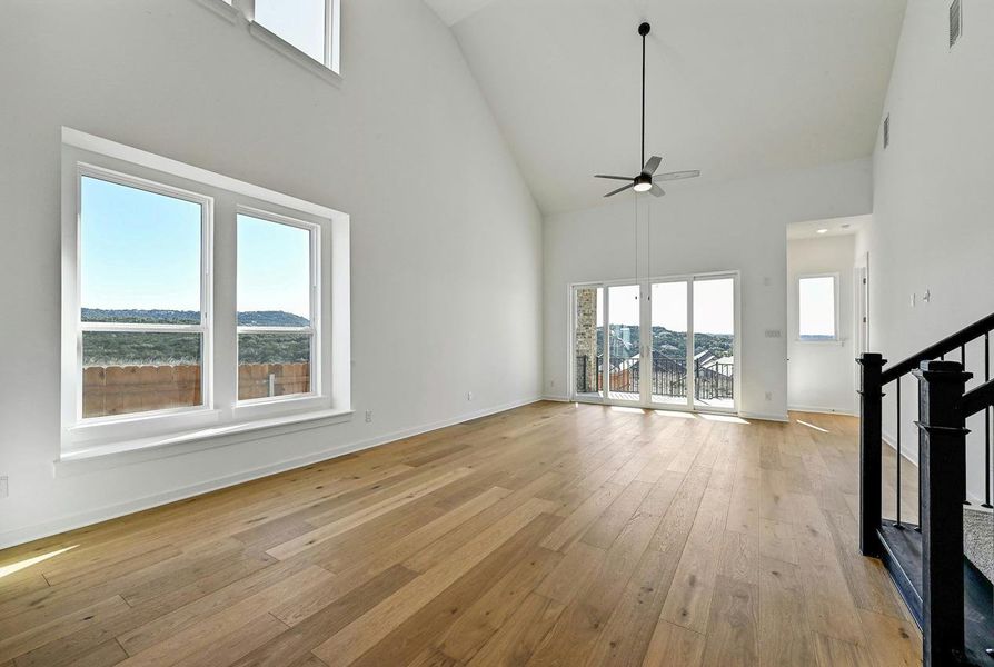 Unfurnished living room featuring high vaulted ceiling, a ceiling fan, light wood-style floors, and stairs