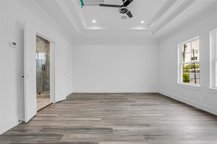 Discover a spacious primary bedroom featuring sleek hardwood floors, abundant natural light from large windows, and an elegant ensuite bathroom with a modern glass shower.