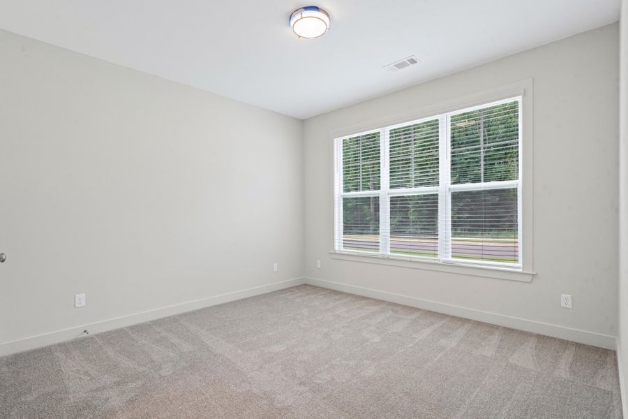 Spacious room featuring light gray carpeting, a multi-pane window with blinds, and neutral wall paint Spacious room featuring light gray carpeting, a multi-pane window with blinds, and neutral wall paint