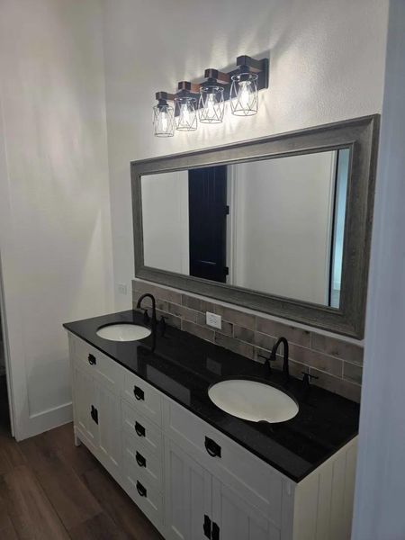 Bathroom with double vanity, dark wood finished floors, and backsplash Bathroom with double vanity, dark wood finished floors, and backsplash
