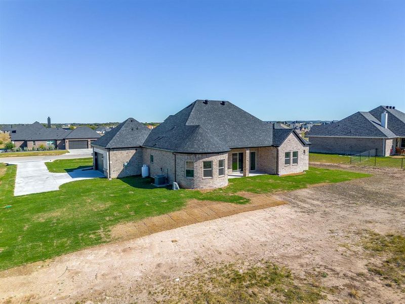 Back of property with a patio area, a shingled roof, brick siding, and a yard
