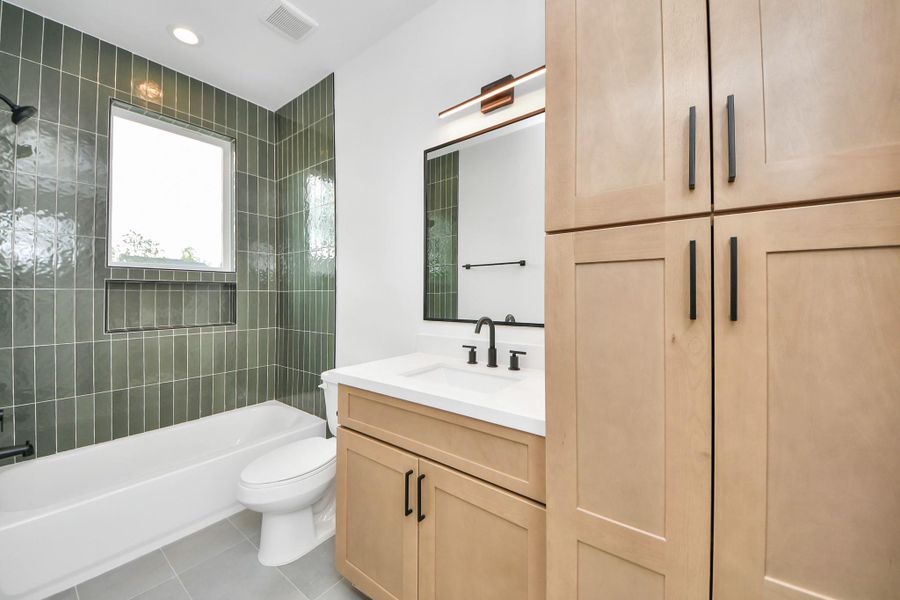 Discover the elegance of this second full bathroom, featuring sleek green tile, modern fixtures, and ample storage for a touch of luxury and functionality.