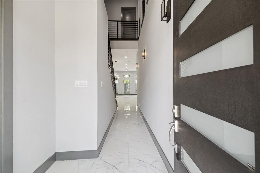 Modern entry sets the tone with porcelain tile floors, crisp lines, and generous natural light. The double-height ceiling and open railing above lead the eye toward the main living areas, establishing a refined sense of arrival.