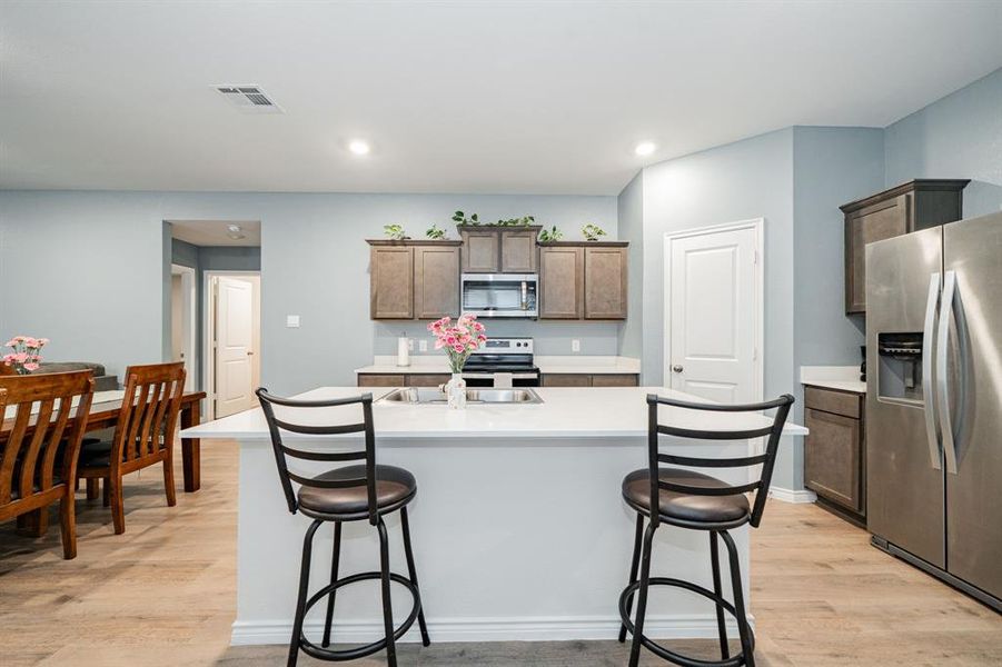 Kitchen featuring appliances with stainless steel finishes, a center island with sink, a breakfast bar area, light wood finished floors, and recessed lighting Kitchen featuring appliances with stainless steel finishes, a center island with sink, a breakfast bar area, light wood finished floors, and recessed lighting
