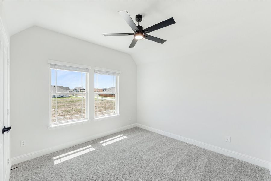Empty bedroom with vaulted ceiling, black ceiling fan, carpet flooring, and two windows with neighborhood view