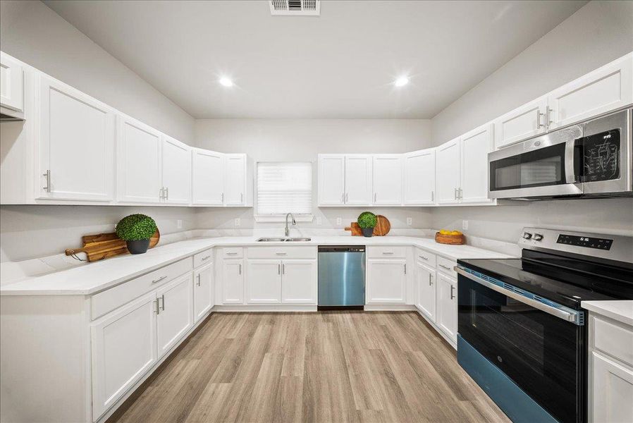 Kitchen with appliances with stainless steel finishes, light wood-style flooring, white cabinetry, and recessed lighting Kitchen with appliances with stainless steel finishes, light wood-style flooring, white cabinetry, and recessed lighting