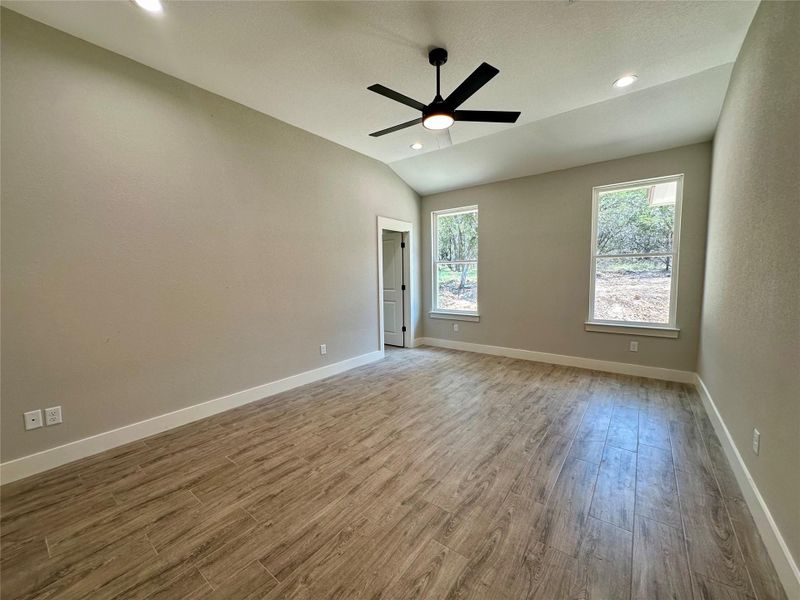 Empty room with wood finished floors, a ceiling fan, vaulted ceiling, baseboards, and recessed lighting Empty room with wood finished floors, a ceiling fan, vaulted ceiling, baseboards, and recessed lighting