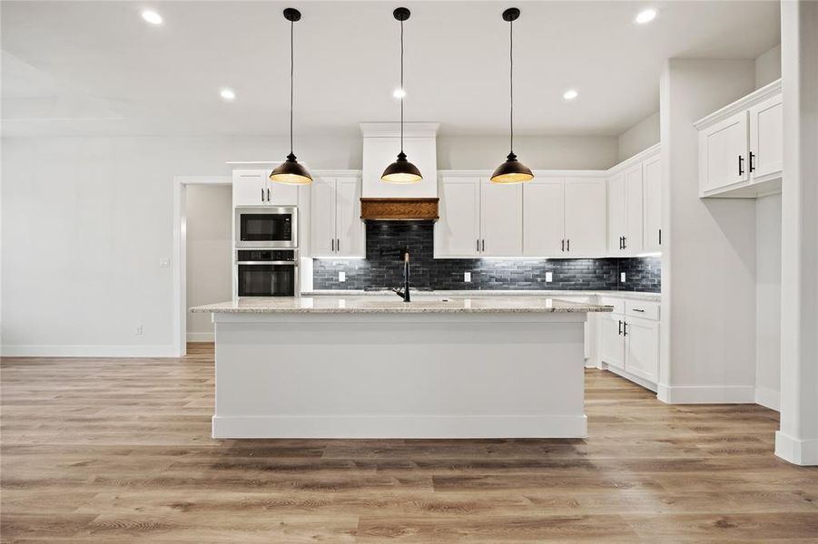 Kitchen featuring white cabinetry, stainless steel appliances, light stone countertops, a kitchen island with sink, and light wood-type flooring