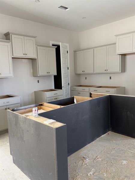 U-shaped kitchen layout with light-toned upper and lower cabinetry, recessed lighting, and a partially constructed dark-toned island U-shaped kitchen layout with light-toned upper and lower cabinetry, recessed lighting, and a partially constructed dark-toned island