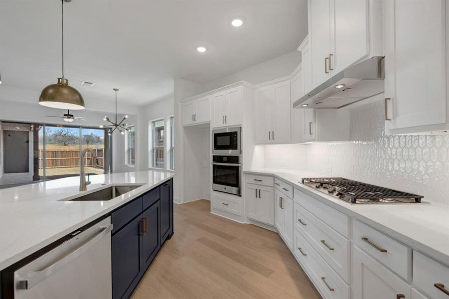 Kitchen with two tone cabinets, stainless steel appliances, light stone counters, light wood finished floors, and a chandelier