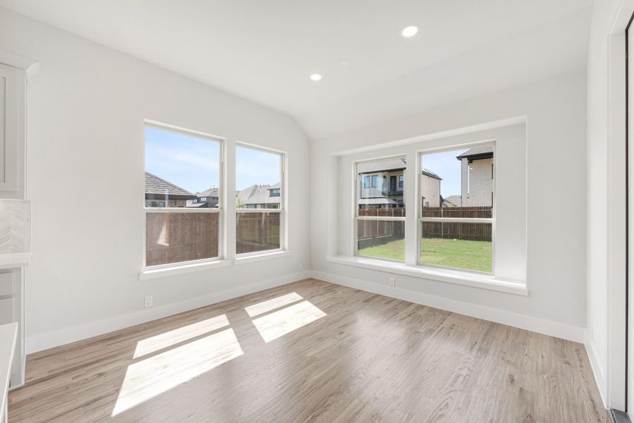 Empty room with light wood floors, vaulted ceiling, and large windows overlooking backyard